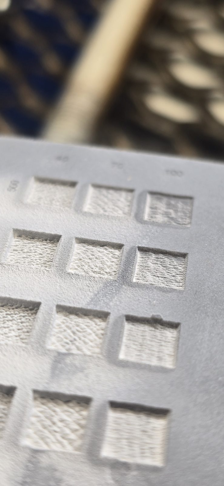 Matriz de grabado ráster en goma gris de 2 mm vista en ángulo: casillas con paredes rectas y polvo blanco