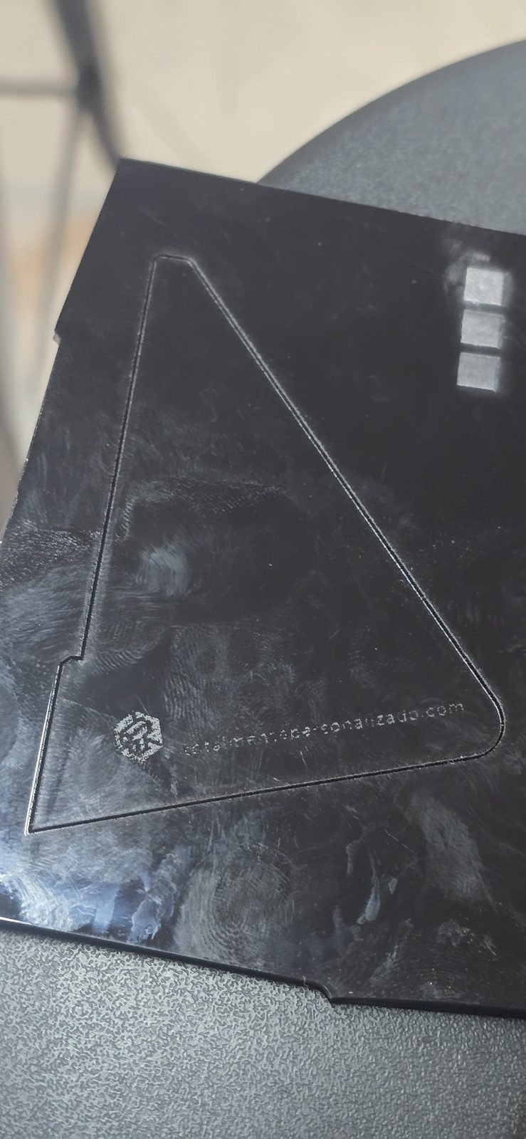 Plancha de metacrilato negro con la silueta triangular de la pata marcada pero sin cortar y el grabado del logo muy flojo