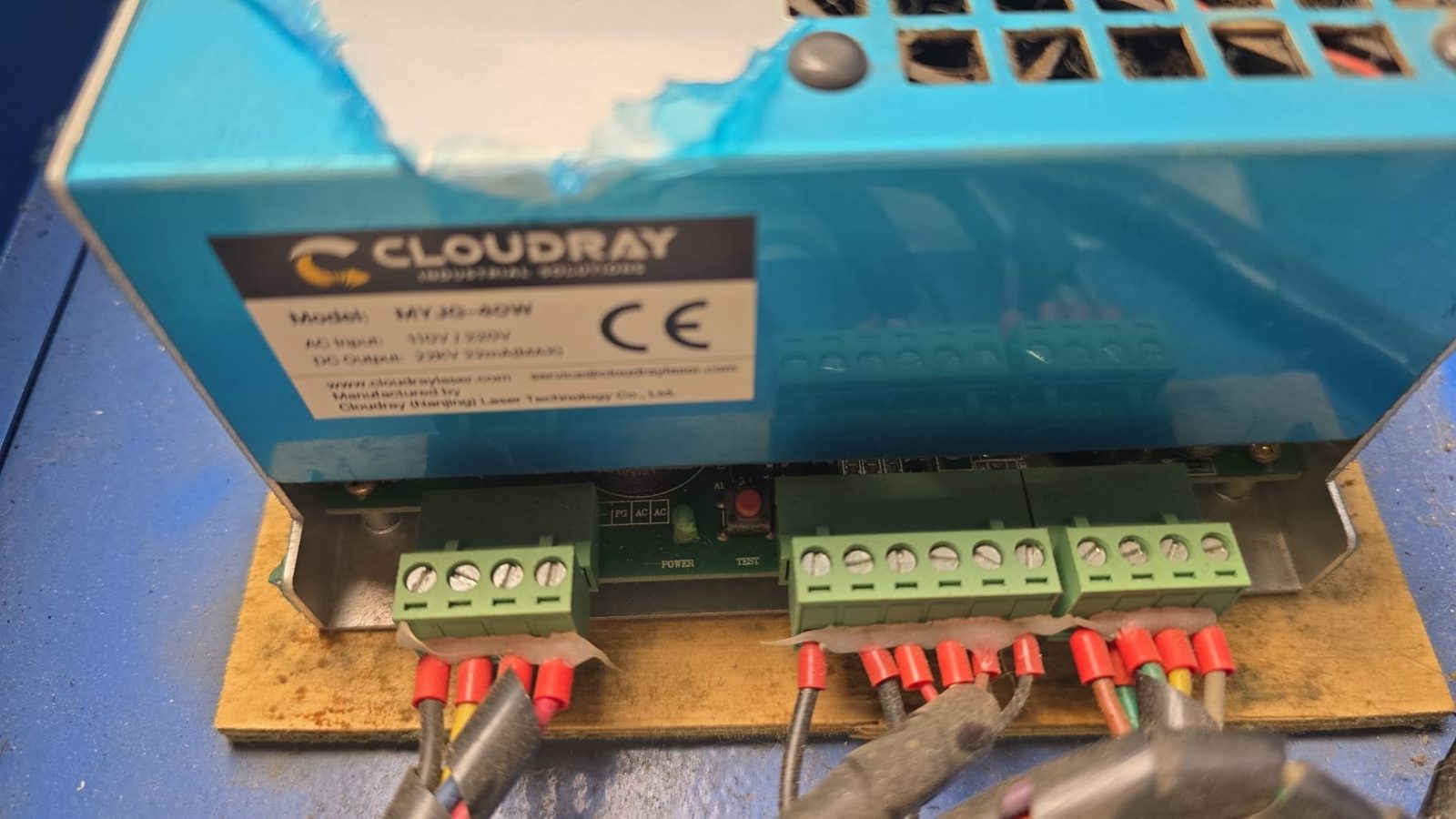 Fuente Cloudray MYJG-40W azul sobre una tabla de madera, con la etiqueta y los tres bloques de bornes verdes cableados con punteras