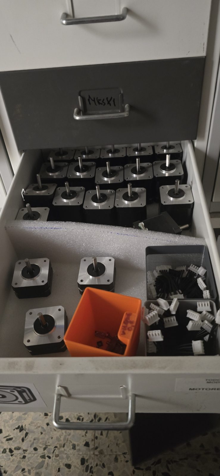 Cajón abierto lleno de motores paso a paso NEMA17 y cables con conectores