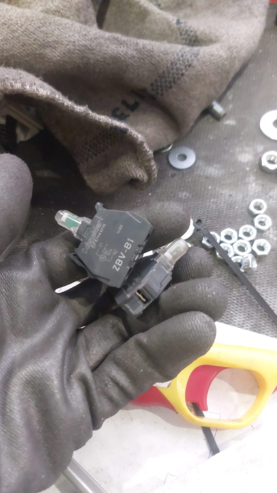 Mano con guante sujetando dos bloques de luz Schneider ZBV-B1 junto a tuercas y arandelas