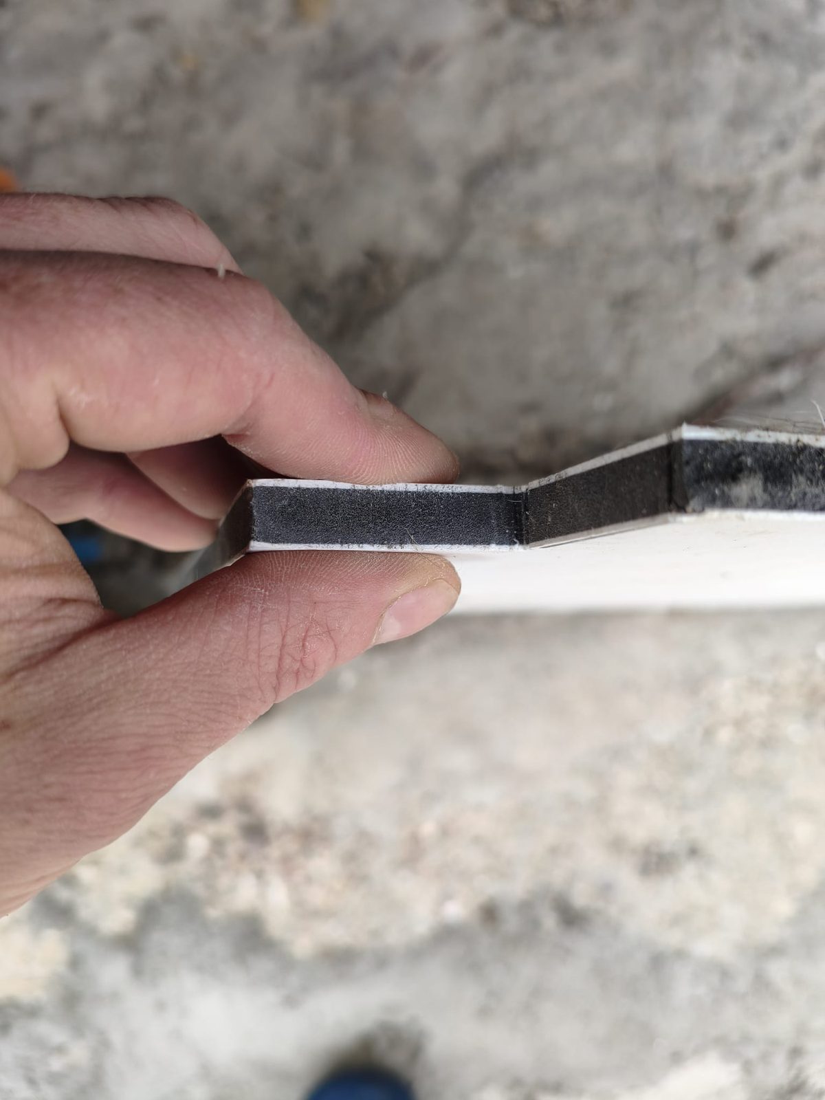 Canto de una placa blanca con el núcleo negro, sujeta con la mano